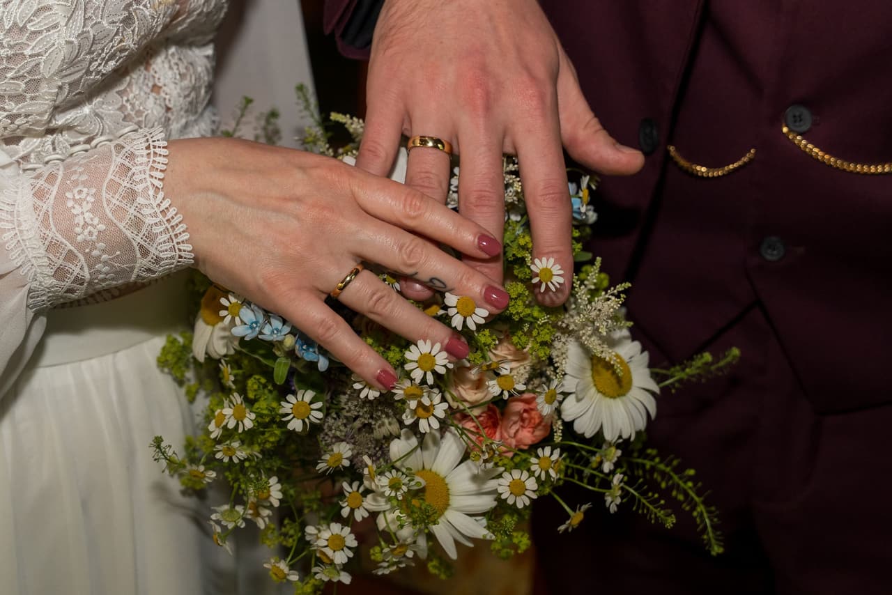 Hochzeit im Standesamt Reinickendorf Berlin, Detailaufnahme der Eheringe und Hände des Brautpaares mit Blumen